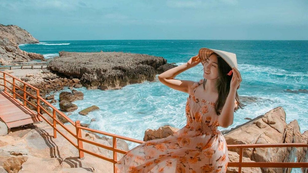 A person in a floral dress standing on a rocky seaside with a wooden staircase and railing. 5