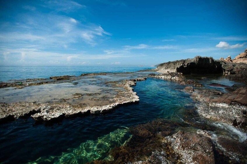 A coastal landscape with clear blue waters, rocky formations, and a distant shoreline. 3