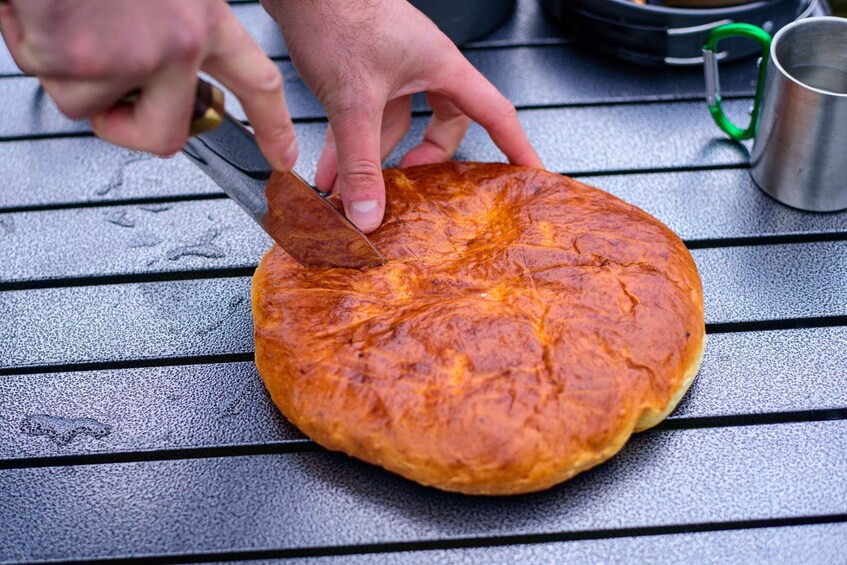 A hand cutting a round, golden-brown baked item on a metal surface. 3