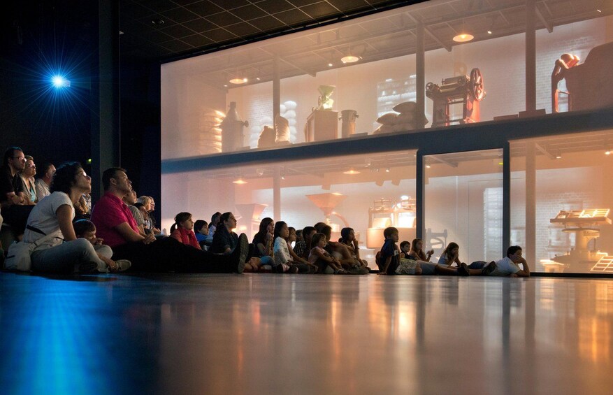 A group of people sitting on the floor watching a projection in a modern building. 4