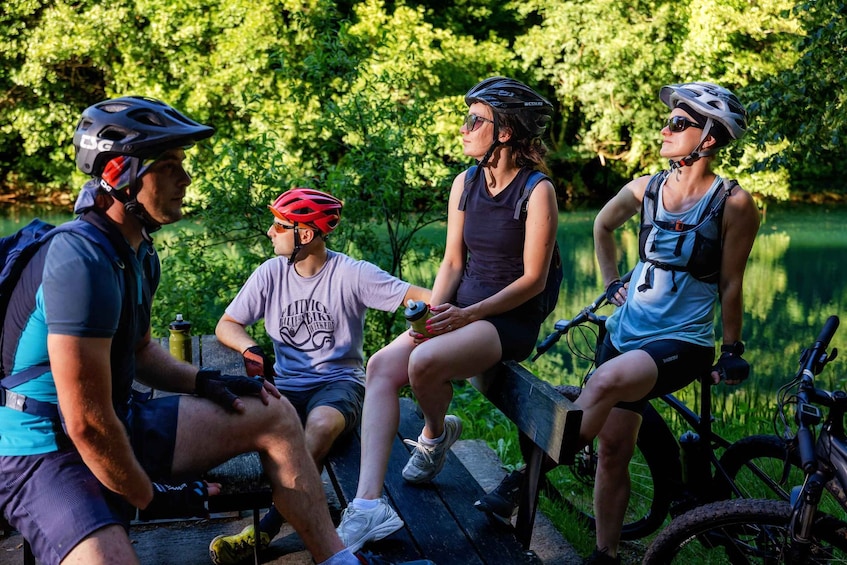 Three cyclists sitting on a bench in a park with trees in the background. 1