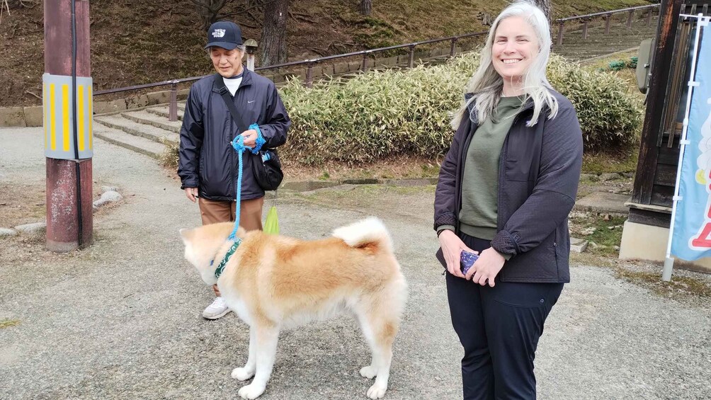 Two people walking a dog on a paved path with grass and bushes in the background. 2