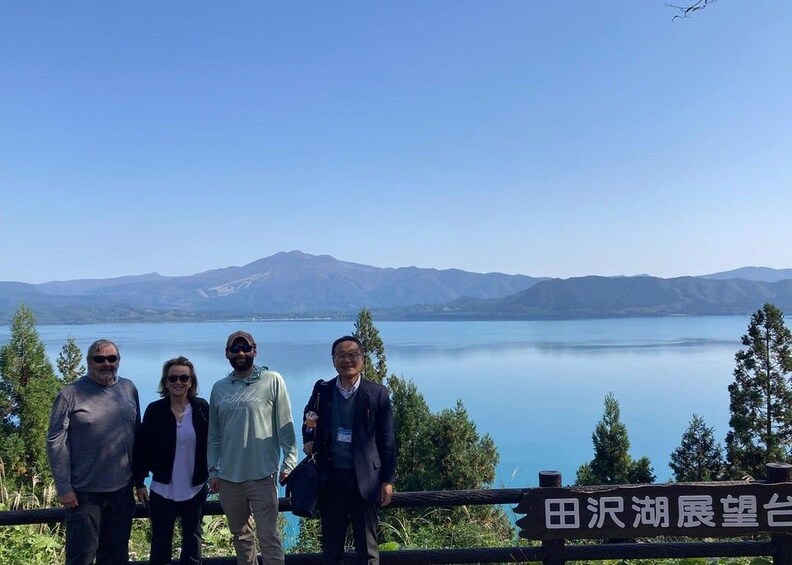 A group of people standing by a railing overlooking a lake with mountains in the background. 5