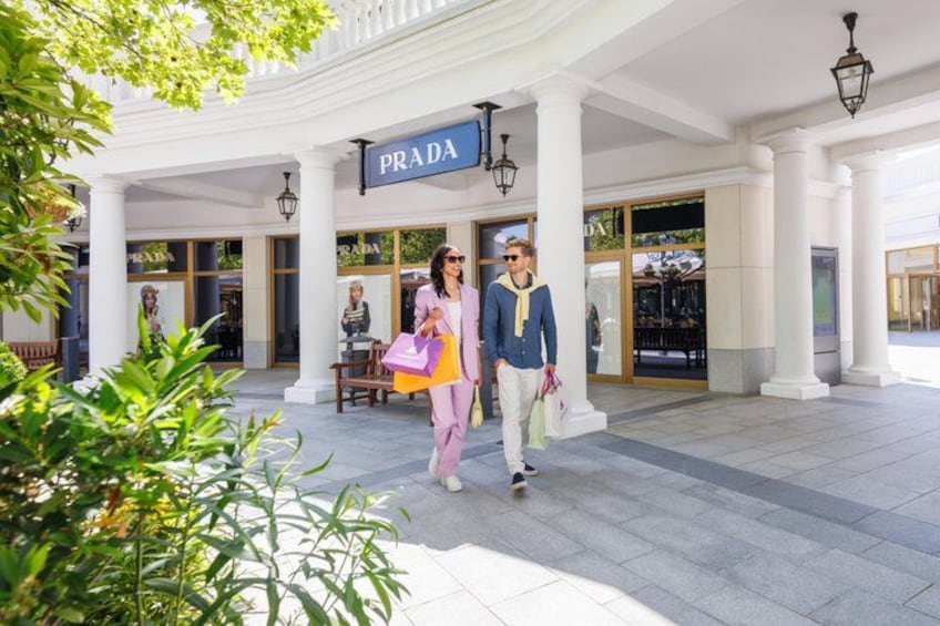 Una pareja caminando frente a una tienda Prada con columnas y un letrero. 1