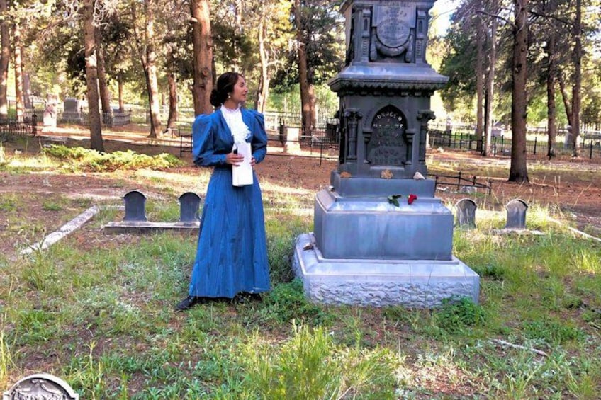 A woman in a blue dress standing next to a gravestone in a cemetery. 3