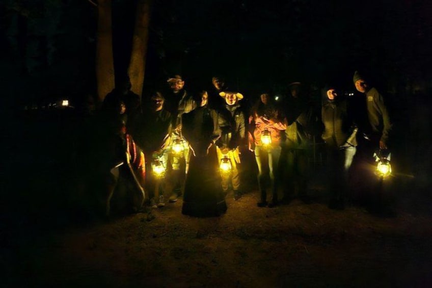 A group of people gathered in a dark outdoor setting, holding illuminated devices. 1