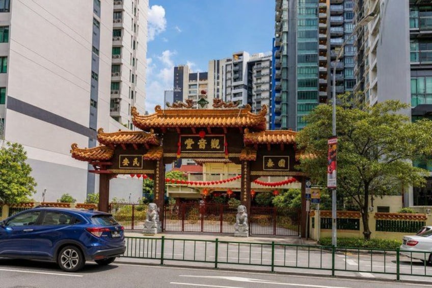 A traditional Chinese gate with ornate decorations, a statue, and a modern urban backdrop with high-rise buildings. 1