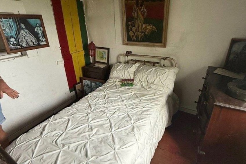 A bed with a quilt, a wooden nightstand with a lamp, and a wall with a framed picture. 3