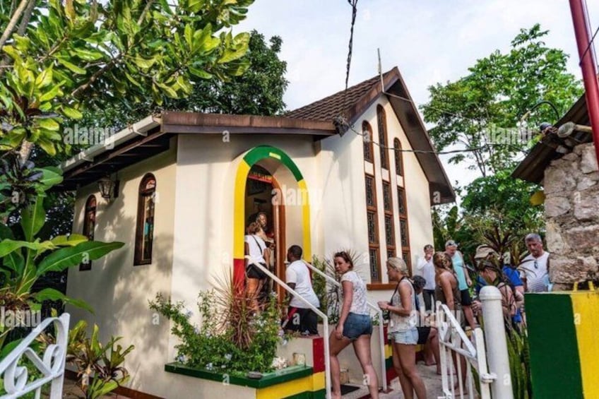 A small church with a green archway, surrounded by greenery and people. 2