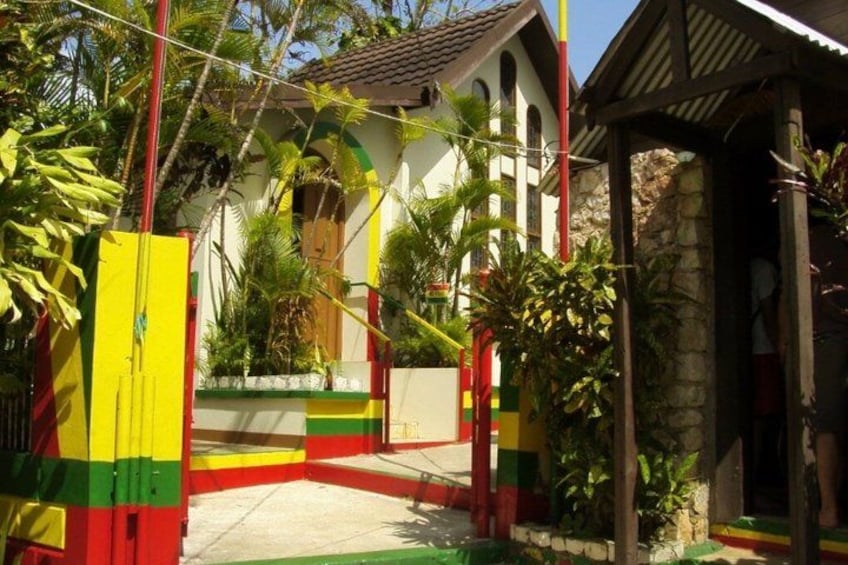 A colorful house with a tiled roof, surrounded by lush greenery and a stone wall. 1
