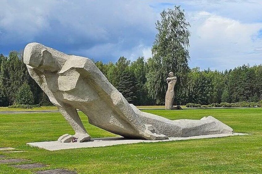 A large stone sculpture of a reclining figure in a grassy field with trees in the background. 4