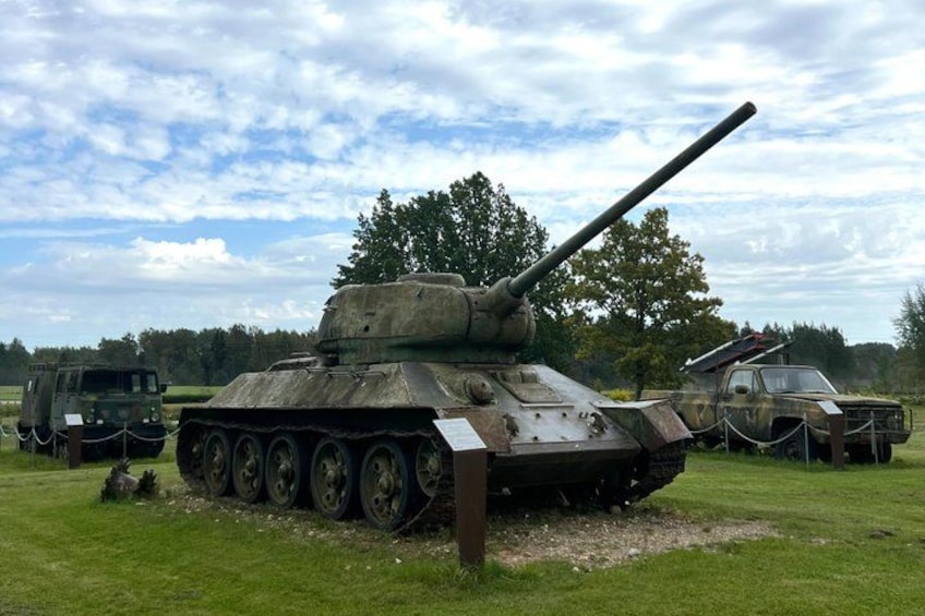 A military tank on display in a grassy field with a truck and a trailer in the background. 1