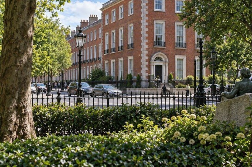 A row of red brick buildings, a tree, a statue, and a street with cars. 2