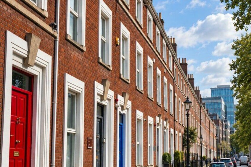 A row of red and blue terraced houses with white window frames and a modern building in the background. 4