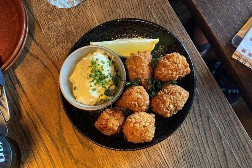 A plate of fried food with a side of sauce and lemon on a wooden table. 4