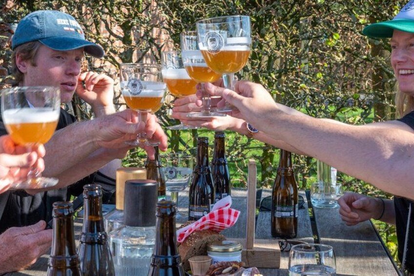 People toasting with beer glasses at an outdoor table with bottles and glasses. 1