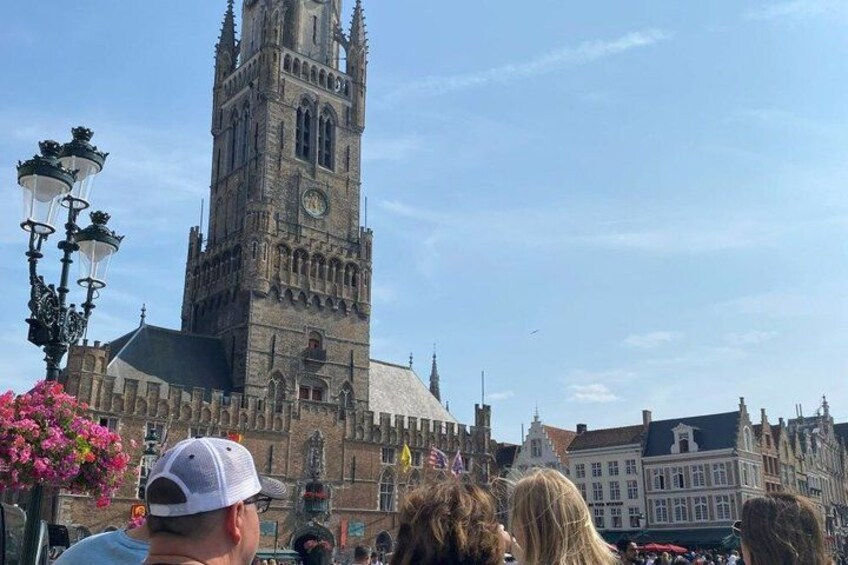 A historic building with a tall tower and a clock, surrounded by other buildings and a crowd of people. 5