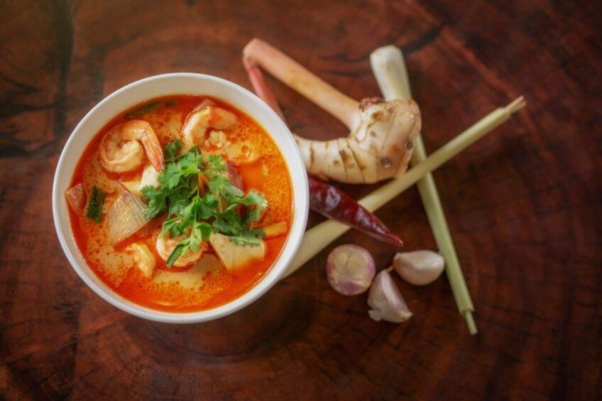 A bowl of soup with shrimp, herbs, and spices on a wooden table. 2
