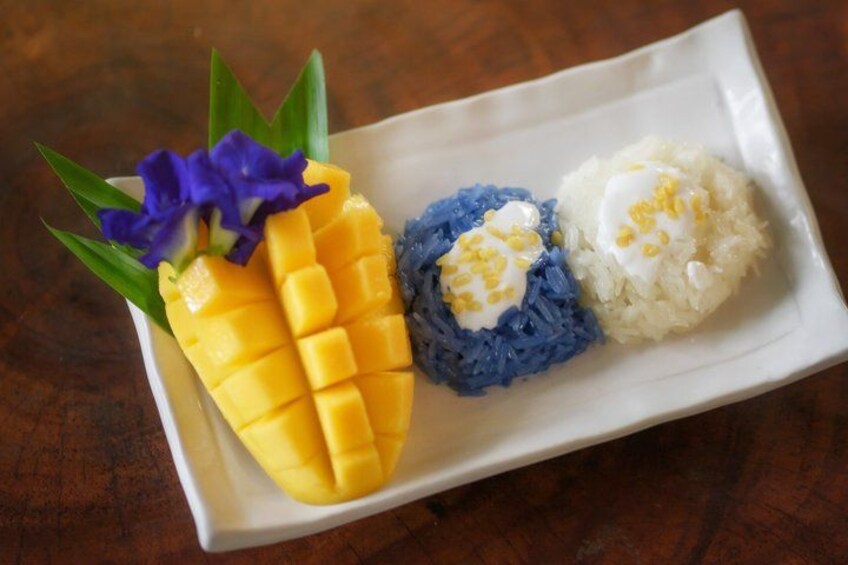 A plate with mango slices, blue-colored rice, and white rice topped with a yellow sauce. 3