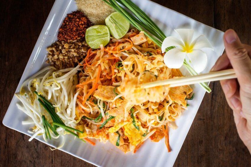 A plate of Pad Thai noodles garnished with bean sprouts, carrots, and green onions, with a flower and lime wedges on the side. 5