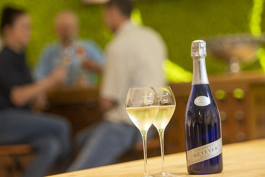 A bottle of champagne and a glass on a table with people in the background. 2
