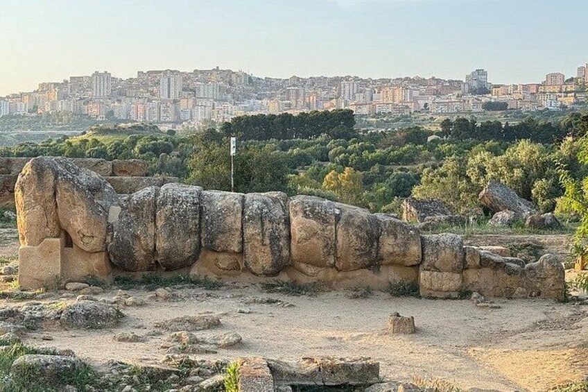 Ancient stone structures, a cityscape in the background, and a clear sky. 2