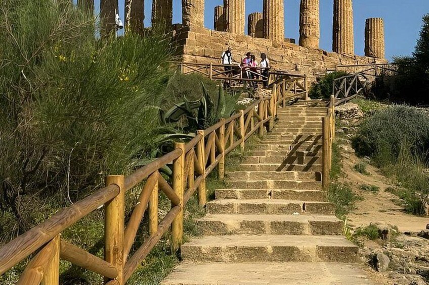 A staircase leading to ancient ruins with a wooden railing, surrounded by greenery. 3