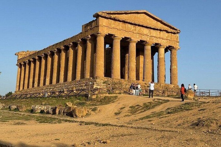 An ancient Greek temple with columns, visitors, and a clear sky. 1