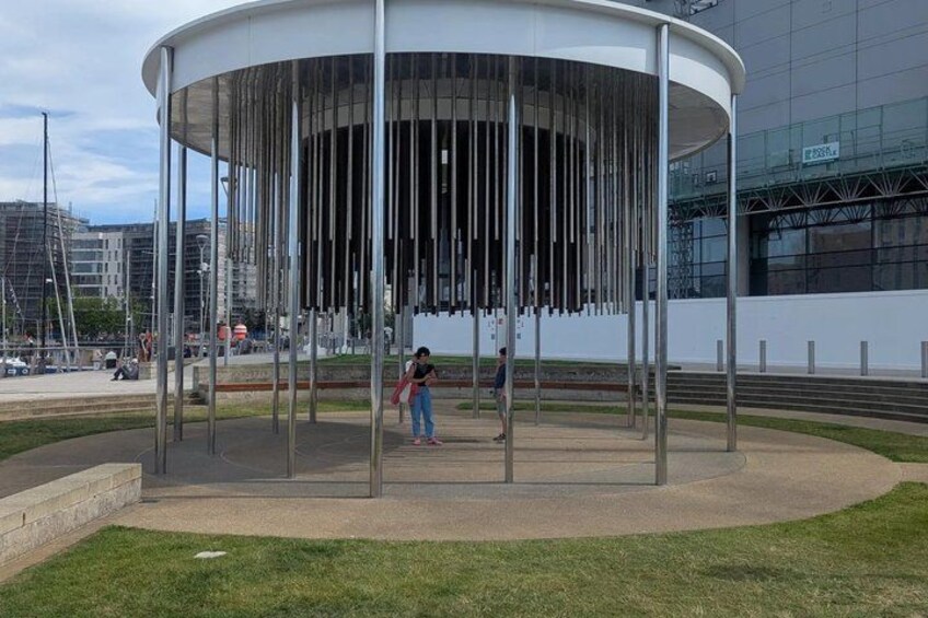 A modern pavilion with vertical slats, a grassy area, and a cityscape in the background. 3