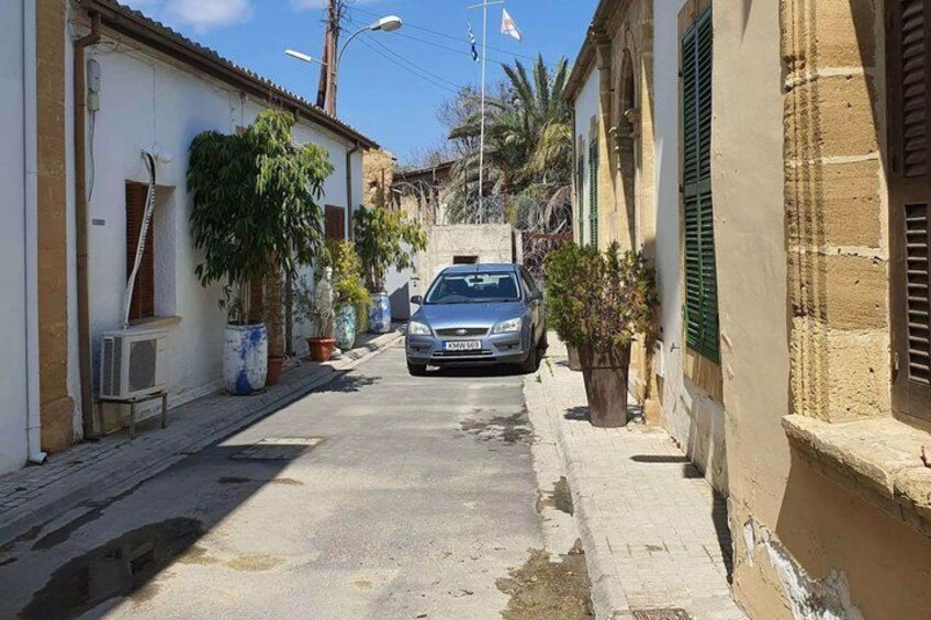 A narrow street with a parked car, potted plants, and traditional buildings. 3