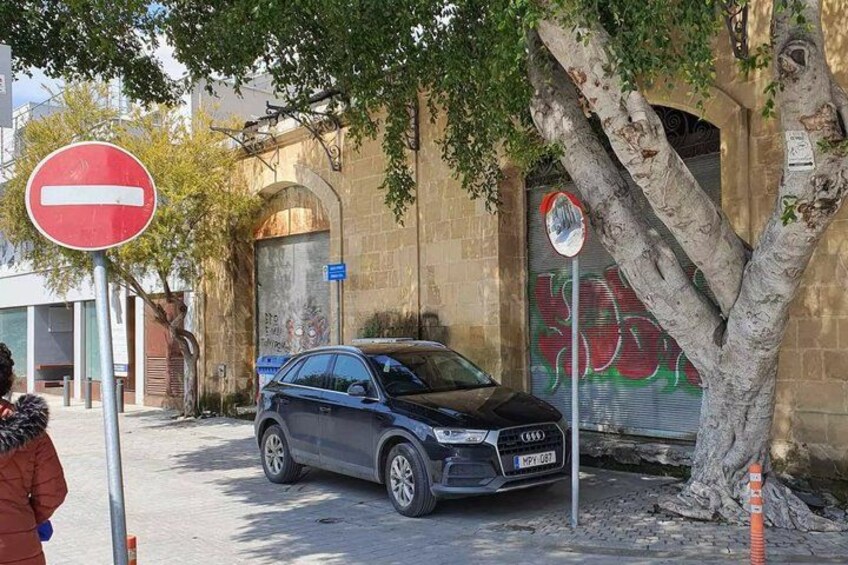 A car parked by a no entry sign, a tree, and a building with graffiti. 5