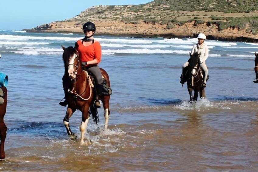 Two people riding horses on a beach with ocean waves in the background. 3