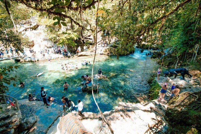 A natural pool surrounded by rocky terrain and trees, with people swimming and enjoying the water. 2