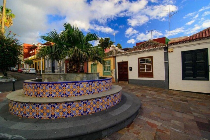 A courtyard with a tiled fountain, palm trees, and traditional buildings. 2