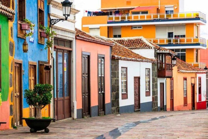 A colorful street with buildings painted in various hues, a black planter with a tree, and a cobblestone pavement. 1