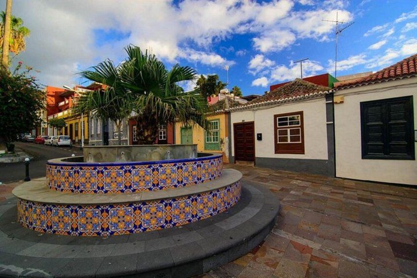 A courtyard with a tiled fountain, palm trees, and traditional buildings. 2