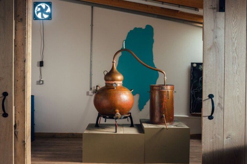 A copper distillation apparatus on a wooden platform with a teal wall in the background. 1
