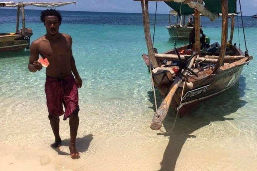 A man standing on a beach with a boat in the water. 1