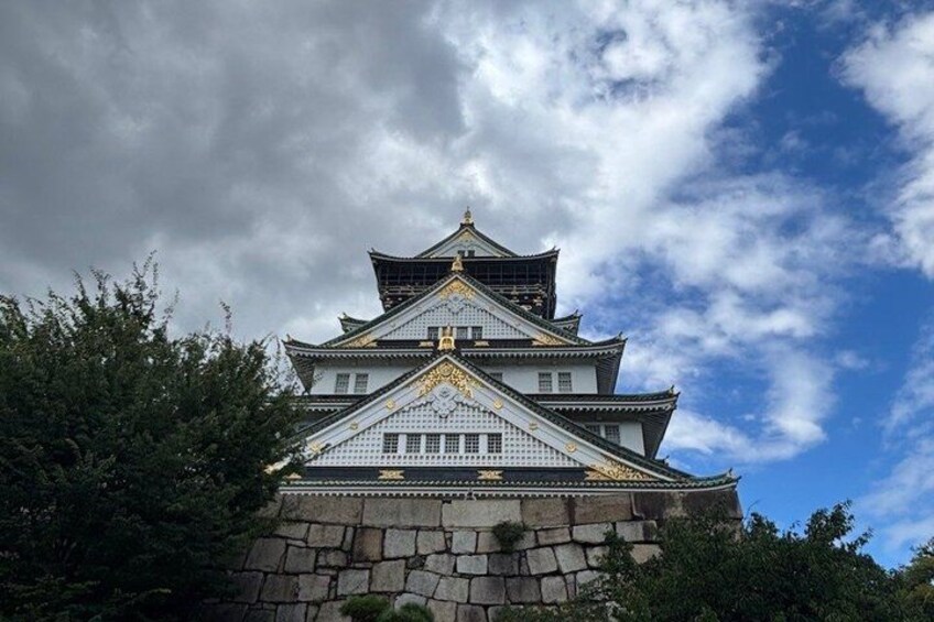 A traditional Japanese castle with multiple tiers, surrounded by greenery and under a partly cloudy sky. 4