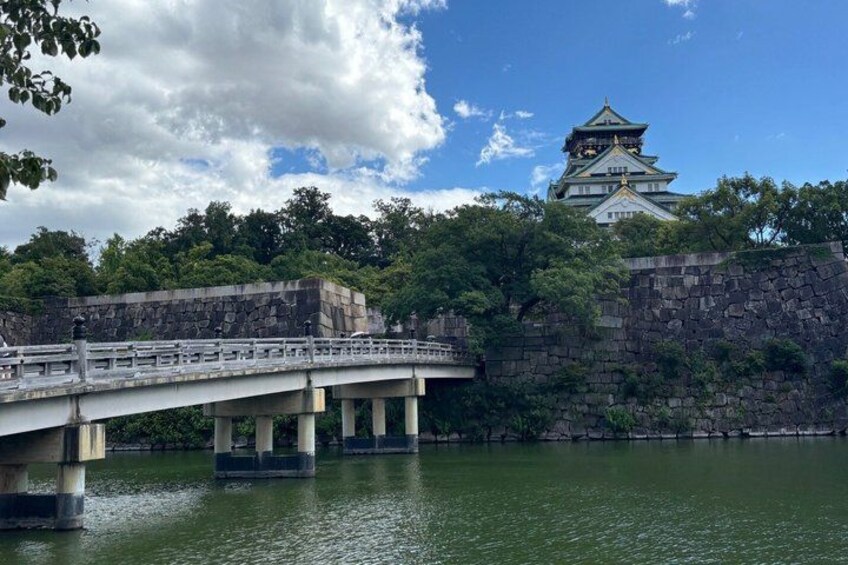 A stone bridge over water, a castle with multiple tiers, and lush greenery. 1