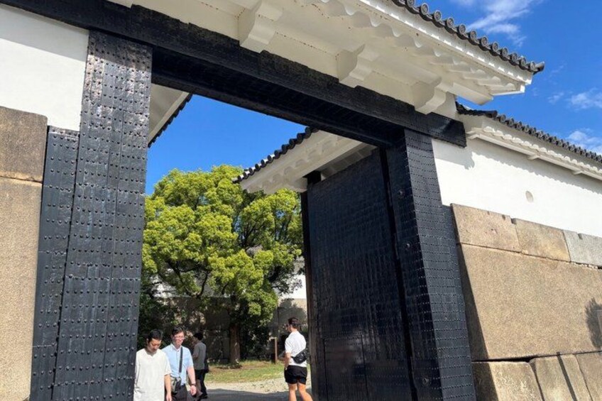 A traditional Japanese gate with a black and white color scheme, a clear blue sky, and green trees in the background. 3