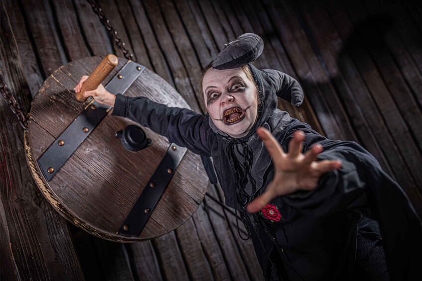 A person in a dark costume with a hat, holding a wooden barrel with metal bands. 2