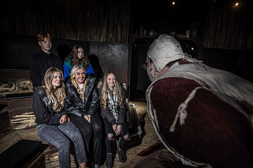 A group of people sitting on a couch in a dimly lit room with a wooden floor and a curtain in the background. 1