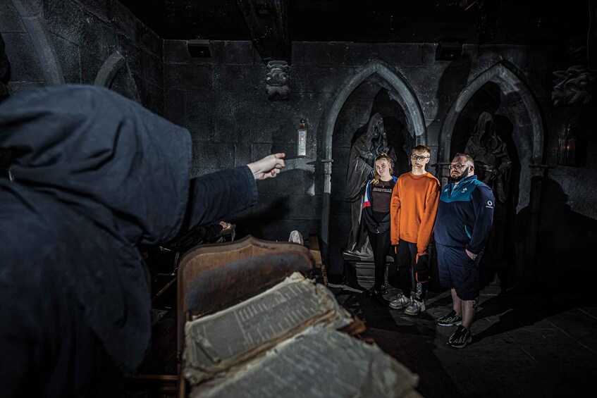A dimly lit stone corridor with arched doorways, a wooden chest, and a person pointing towards something off-camera. 5