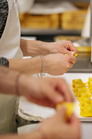 A person preparing food, specifically cutting yellow dough. 4
