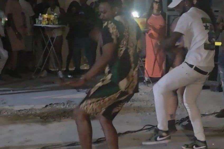 A person in a patterned outfit performing on a stage with an audience in the background. 1