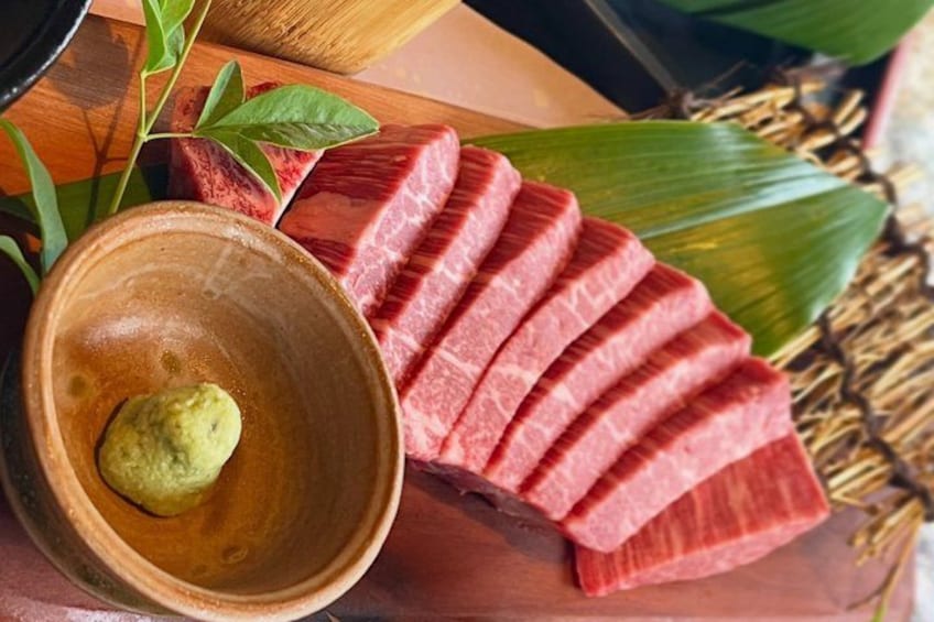 A wooden cutting board with sliced meat and a bowl of green sauce. 1