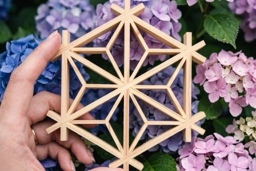 A hand holding a wooden geometric structure with a background of purple hydrangea flowers. 5