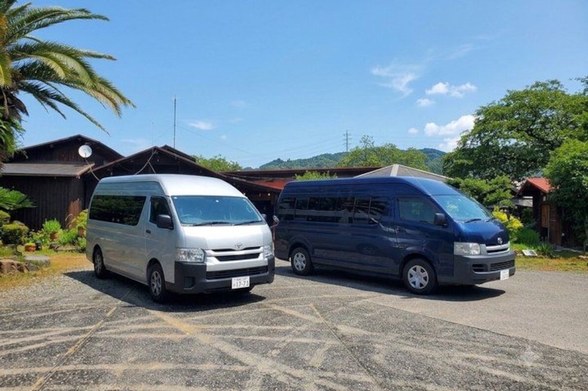 Two vans parked in a lot with a building and trees in the background. 2