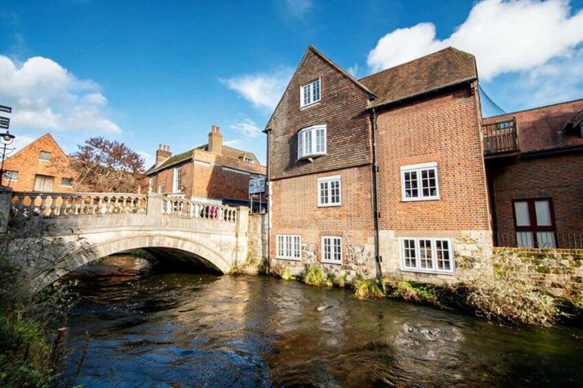 A stone bridge over a narrow waterway, brick buildings, and a clear blue sky. 5